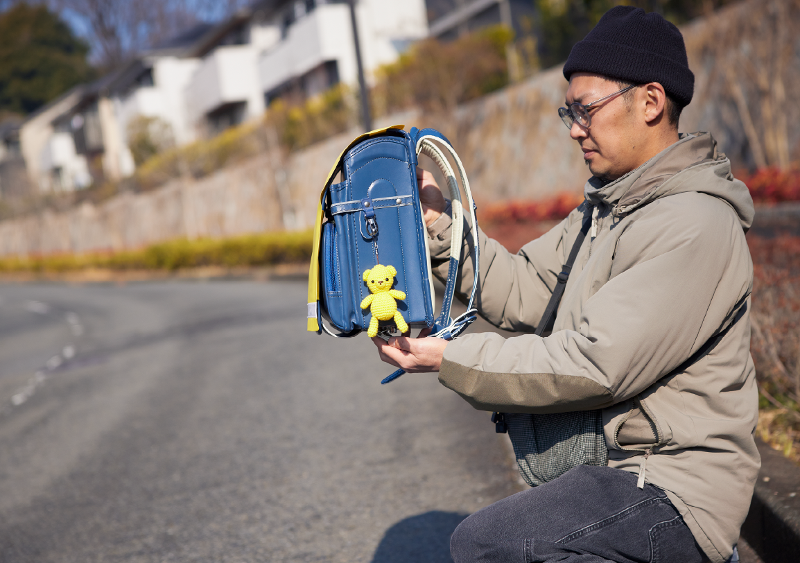黄色いぬいぐるみをランドセルに取り付ける男性の写真