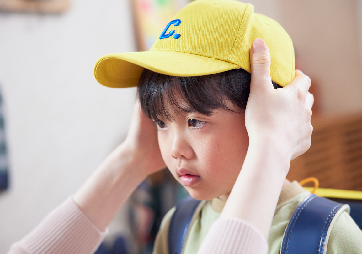 子どもに黄色の帽子をかぶせる母親の写真