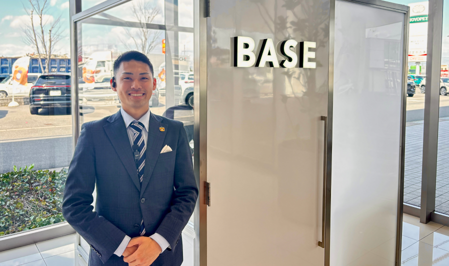 スーツの男性が「BASE」と表示されたドアの前に立つ写真