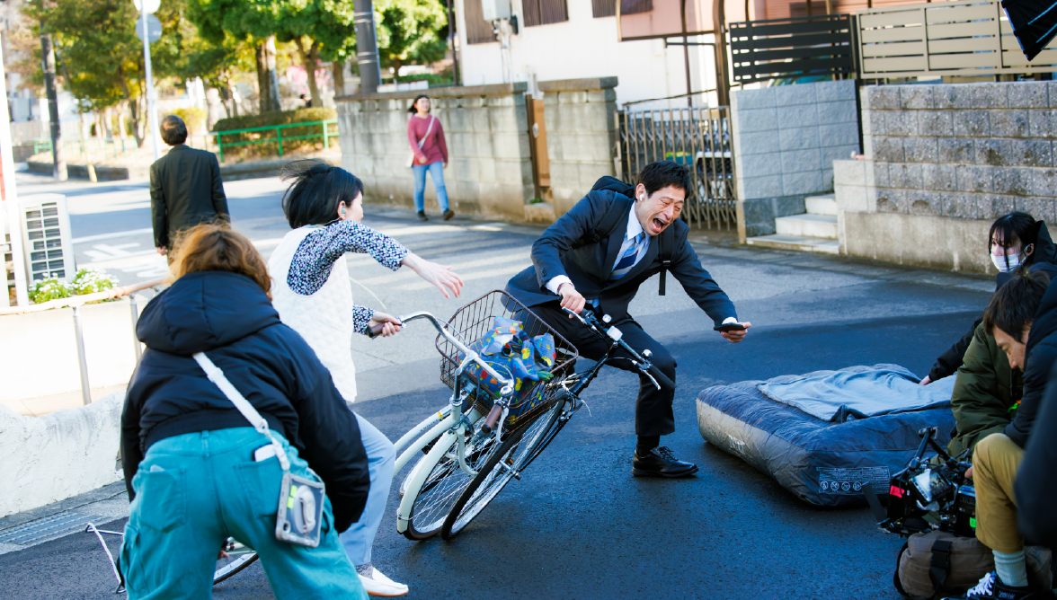 メイキング風景:自転車の接触シーン、男性が転けるところ、道路にはマットが置かれている